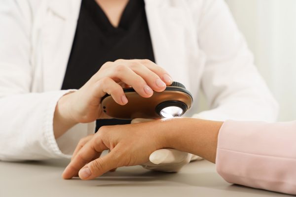 Doctor and client woman in dermatology clinic. Dermatologist is using dermatoscope for skin examination.