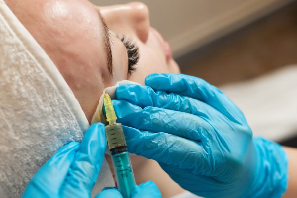 Syringe with a patient's blood plasma in a cosmetologist's hand for a plasmolifting of a woman's facial skin. Plasma therapy, skin cell restoration