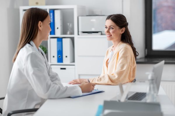 medicine, healthcare and people concept - female doctor with clipboard talking to smiling woman patient at hospital