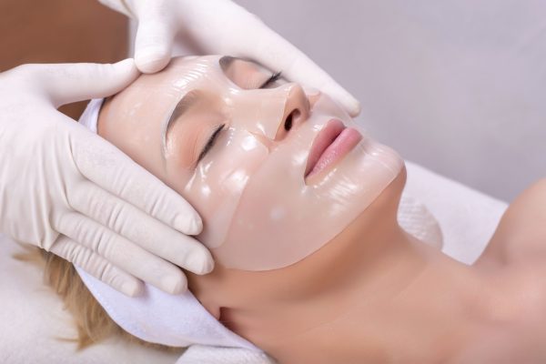 A young female getting skin mask treatment on her face with massage glove